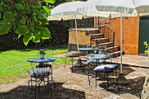 Una terrazza esterna con tavoli e sedie, un'area salotto coperta e una scala che conduce a un livello superiore.