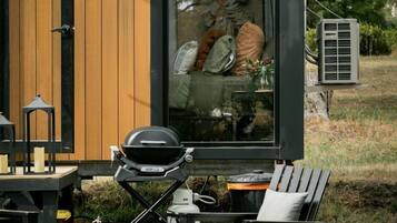 A modern outdoor seating area with a fire pit, a grill, and a view of a cozy interior.