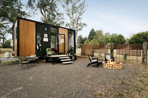 A modern, compact cabin with a wooden exterior, a patio area with outdoor seating, and a fire pit.