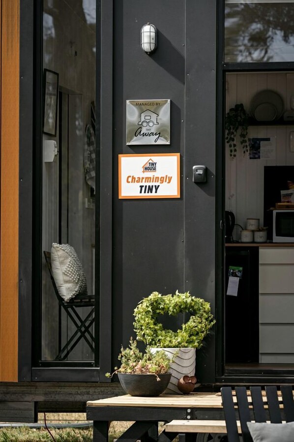 A black exterior wall with a sign indicating 'Charmingly Tiny' and a 'Managed by Away' sign. There is a potted plant on the ground.