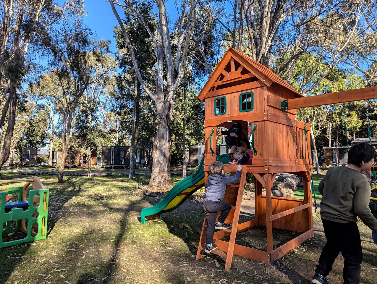 A wooden play structure with a slide and climbing area in a park.