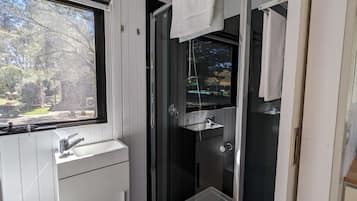 A bathroom with a glass shower enclosure, a sink, and a window.