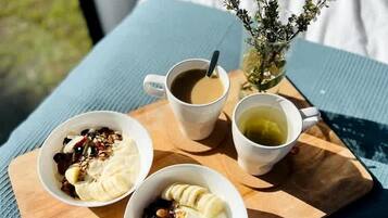 A wooden tray with three bowls of yogurt and granola, a cup of coffee, and a cup of tea, accompanied by a small vase of flowers.