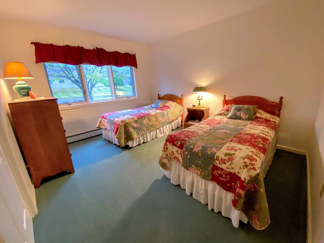 Une chambre avec deux lits, une commode, une fenêtre donnant sur un beau paysage et une lampe.