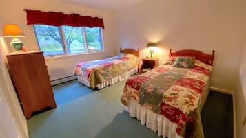Une chambre avec deux lits, une commode, une fenêtre donnant sur un beau paysage et une lampe.