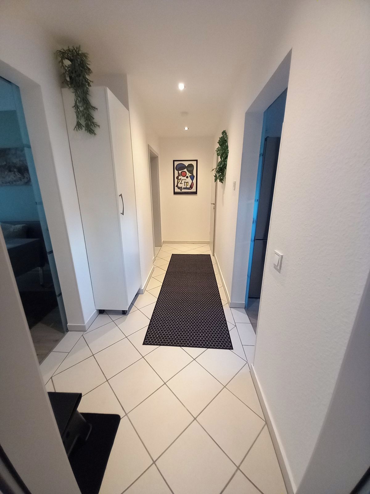 Ein Flur mit weißen Wänden, einer schwarzen Matte und einem gerahmten Kunstwerk an der Wand.