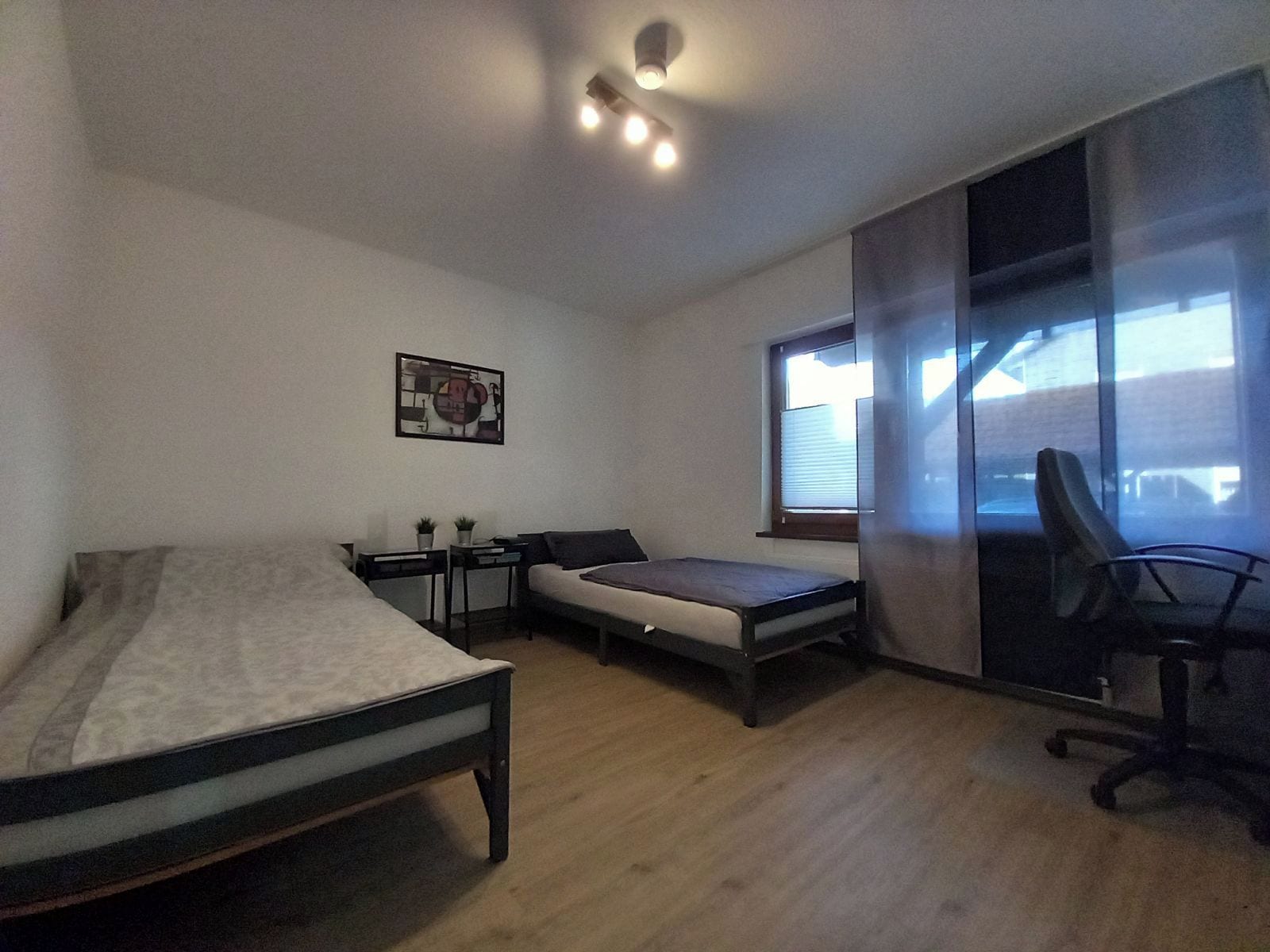Ein Schlafzimmer mit zwei Betten, einem Schreibtisch, einem Stuhl und einem Fenster.