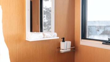 A bathroom with a wooden wall, a white sink with a faucet, a mirror, a window, and a toilet paper holder.