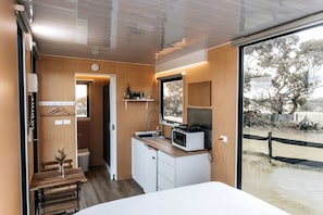 A compact room with a bed, a kitchenette, a window, and a view of the outdoors.
