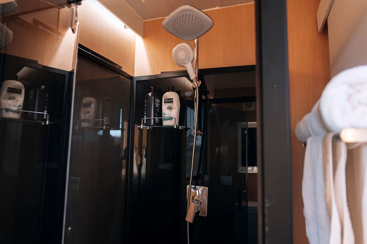 A modern bathroom with a glass-enclosed shower, a handheld showerhead, and a towel rack with a towel.