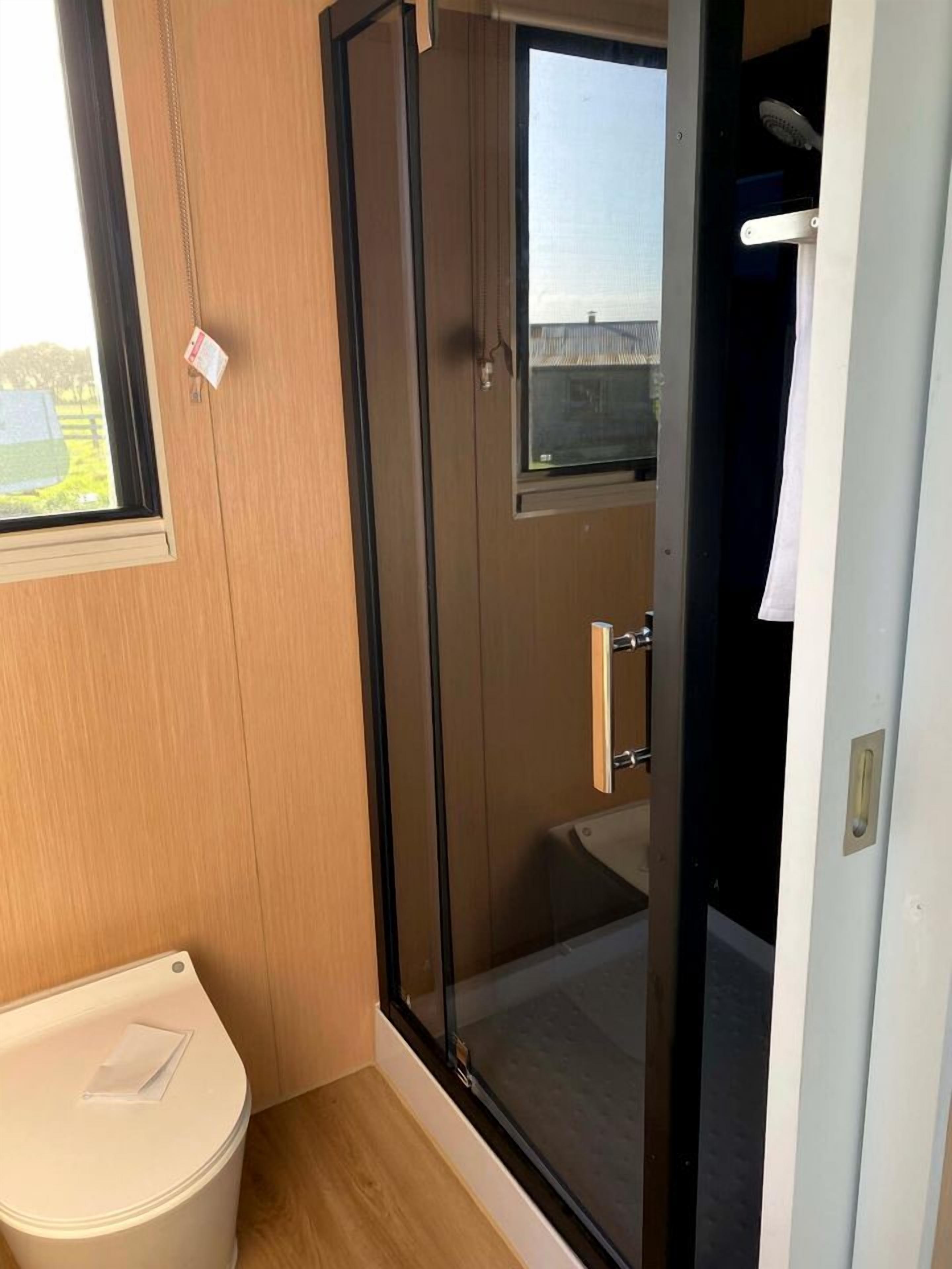 A bathroom with a glass shower enclosure, a toilet, and a window.