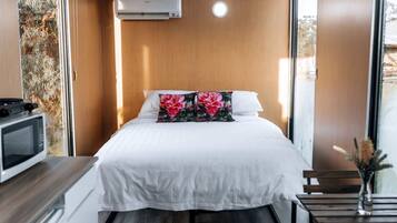 Habitación de hotel compacta con cama, un escritorio pequeño con microondas, ventana con vistas y aire acondicionado instalado en la pared.