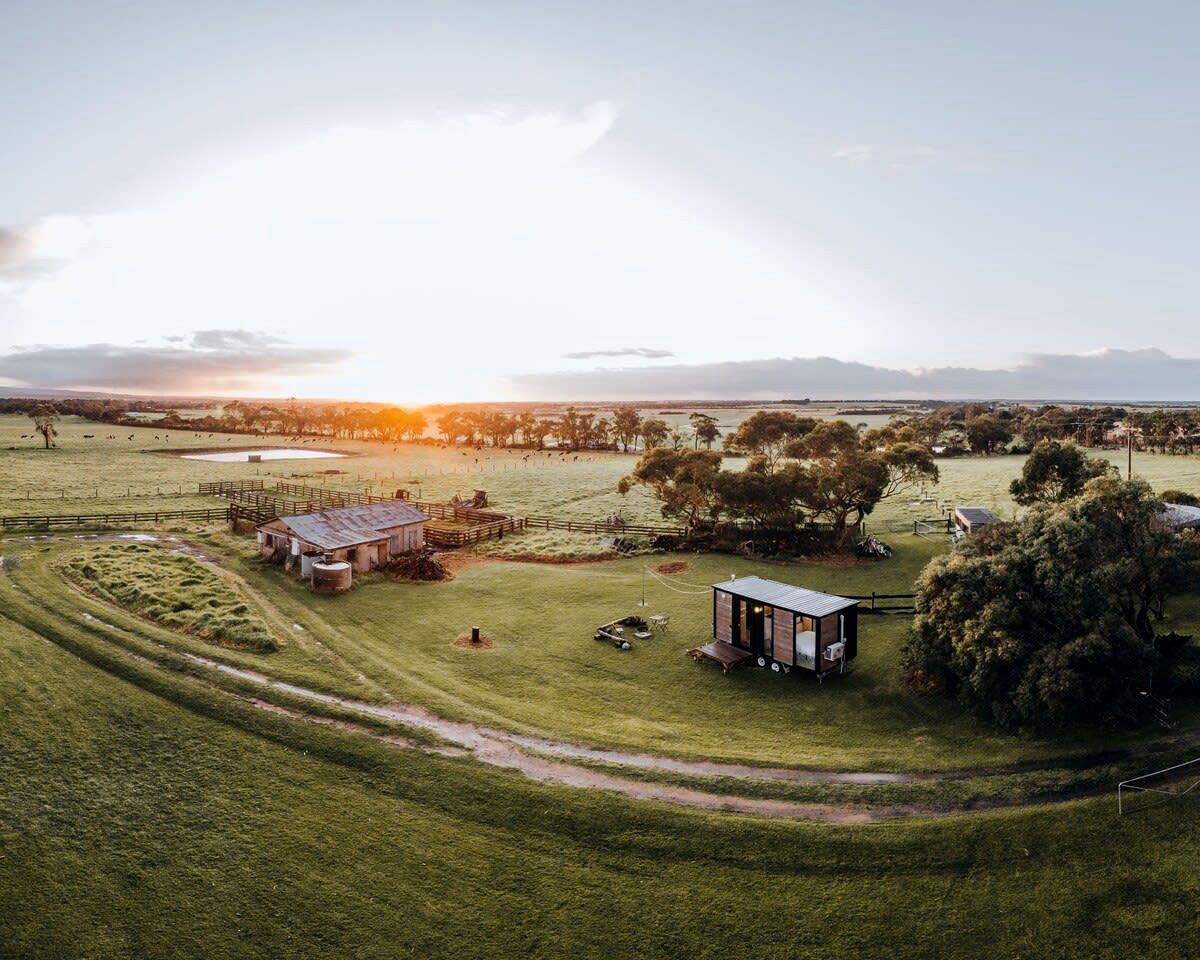 An aerial view of a rural property with a barn, a small cabin, and a fenced pasture.