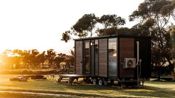 A small, modern mobile home with a sliding door, a flat roof, and a portable air conditioning unit.