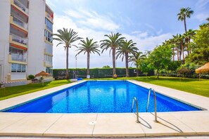 A swimming pool with a clear blue water surface, surrounded by a well-maintained lawn and palm trees. - Apartment in Nerja by Torrecilla Beach (Nerja)