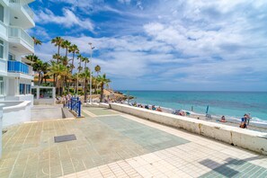 A beachfront hotel with a paved walkway, palm trees, and a view of the ocean. - Apartment in Nerja by Torrecilla Beach (Nerja)