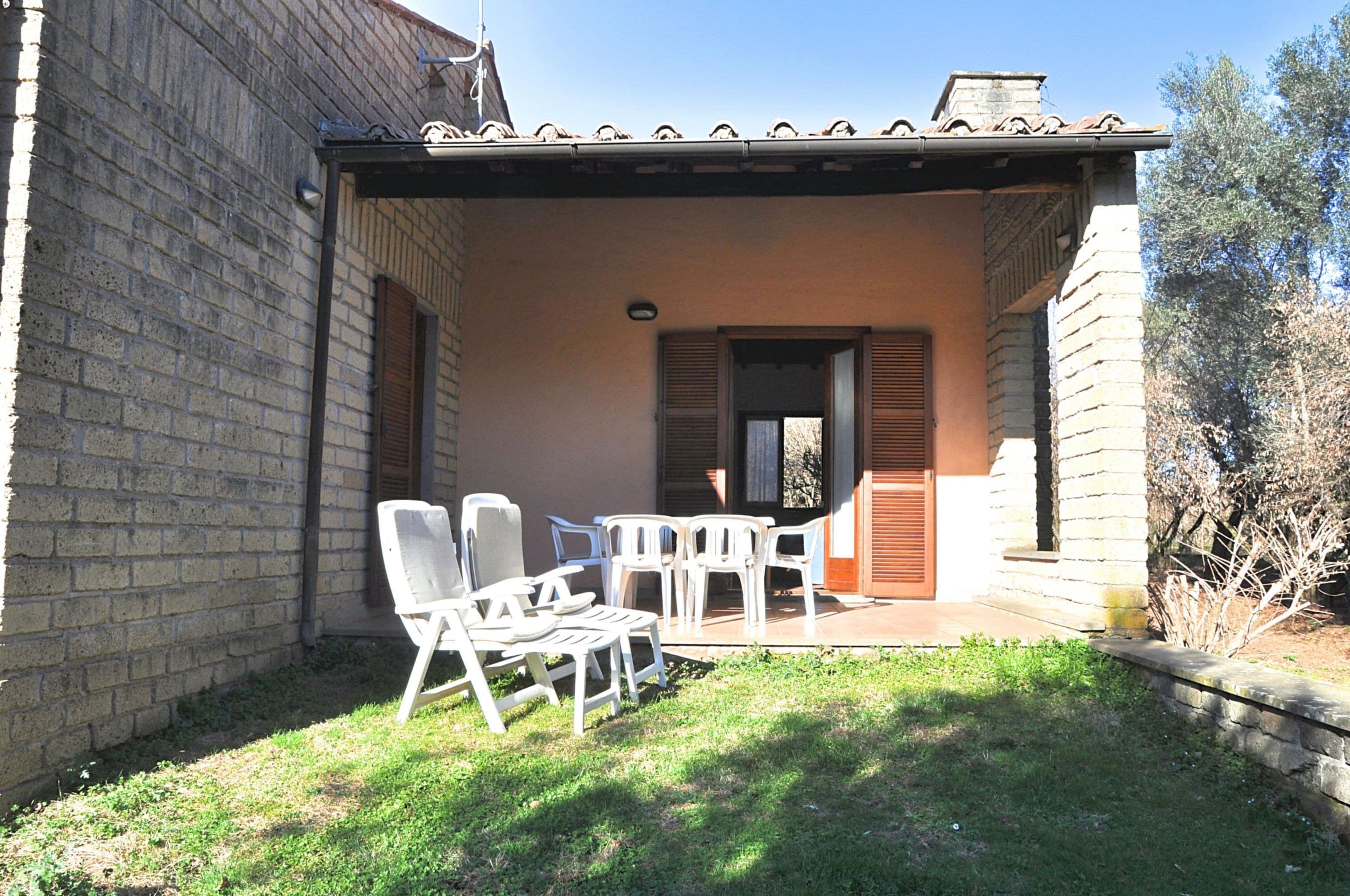 A covered outdoor seating area with a brick wall, a tiled roof, and a small garden.