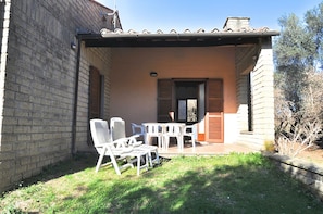 A covered outdoor seating area with a brick wall, a tiled roof, and a small garden. - Montecasciano Primula (Capranica)