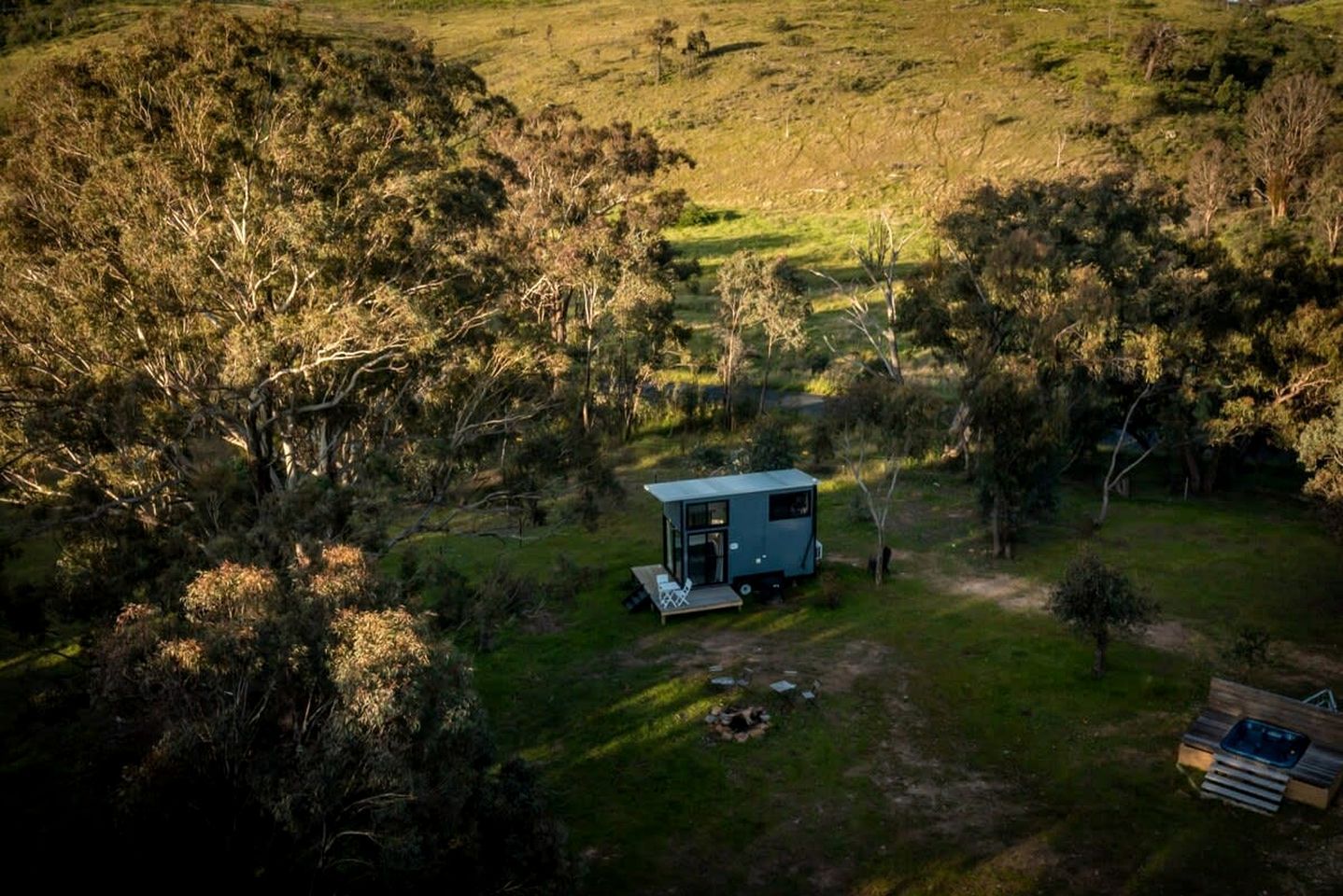 A remote, single-story cabin with a porch, surrounded by dense woodland.
