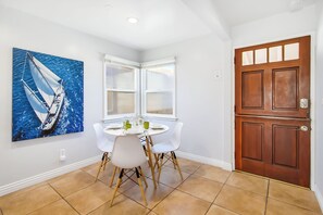 A dining area with a white table, four chairs, and a painting of a sailboat on the wall. - Short Walk To Sand, Prefect for Families, Large Deck! (Newport Beach)