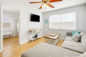 A modern living room with a flat-screen TV, a ceiling fan, a wooden coffee table, and a sofa. - Short Walk To Sand, Prefect for Families, Large Deck! (Newport Beach)