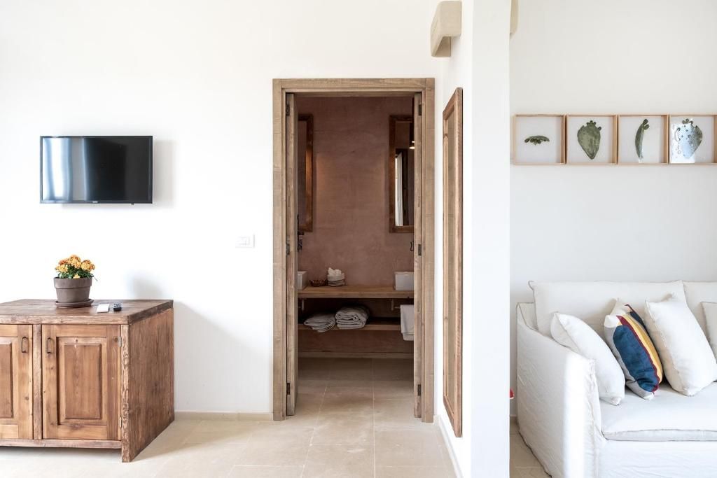 Una habitación con un armario de madera, un televisor montado en la pared, un sofá blanco con cojines y una puerta que da a un vestidor con estantes.