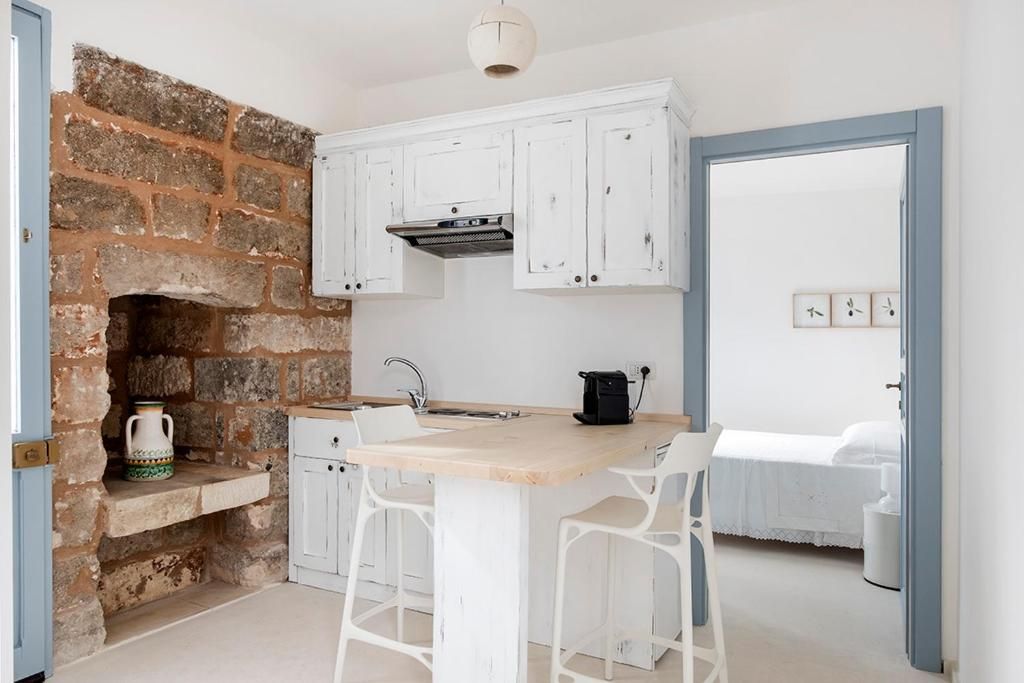 A kitchen with white cabinets, a brick wall, a wooden countertop, and two white bar stools.
