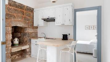 A kitchen with white cabinets, a brick wall, a wooden countertop, and two white bar stools.