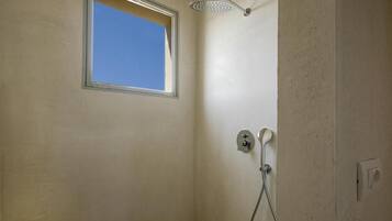 A bathroom with a shower, a window, and a wall-mounted light fixture.