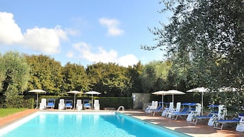 A swimming pool with lounge chairs and umbrellas, surrounded by greenery.