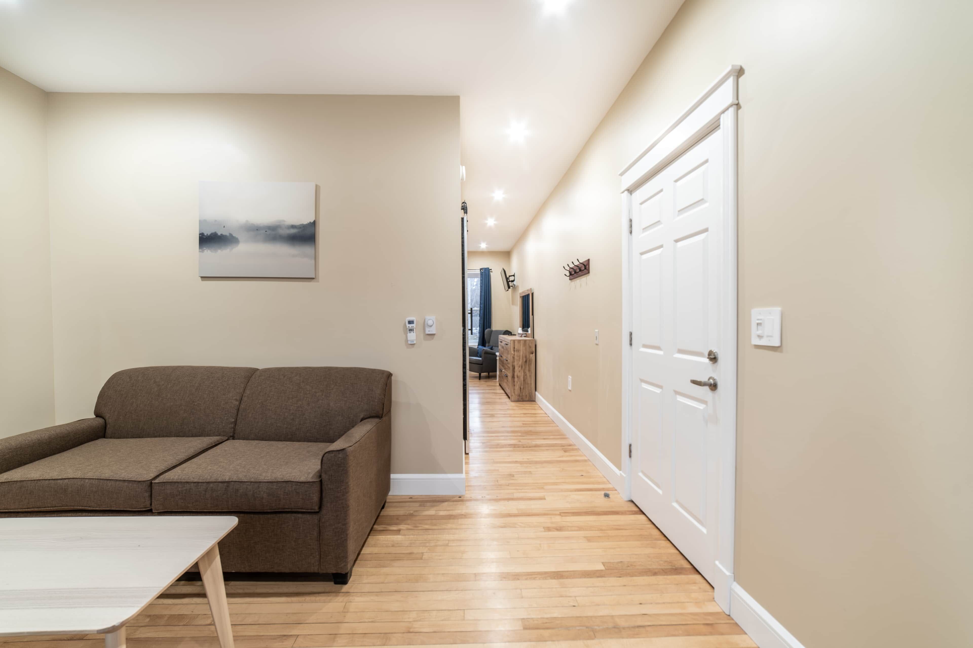 A hallway with a wooden floor, a brown sofa, a white table, and a white door.