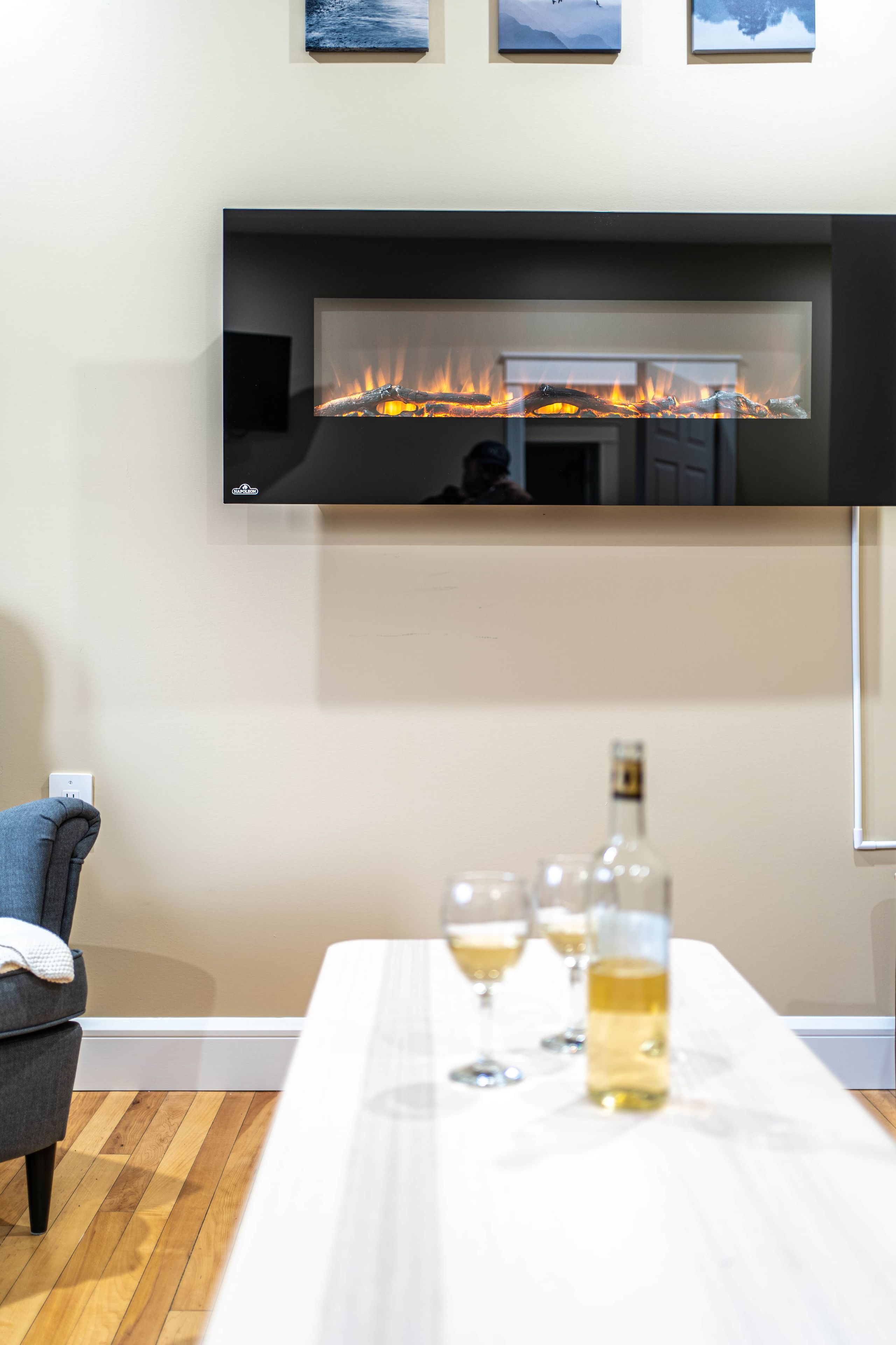A modern living room with a fireplace, a dining table with glasses and a bottle, and a gray armchair.