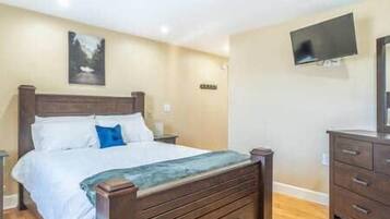 Ein Schlafzimmer mit einem Bett, einem Schminktisch, einem Fernsehgerät an der Wand und einem Bild über dem Bett.
