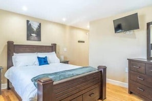Une chambre à coucher avec un lit, une commode, un téléviseur fixé au mur et un tableau au-dessus du lit.