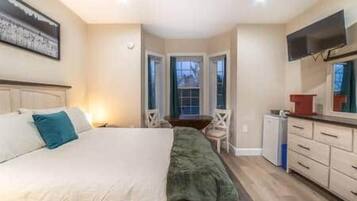 Quarto com cama, escrivaninha, cadeira e televisão.