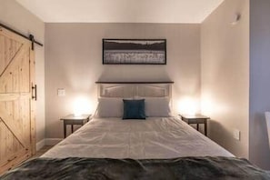 Un dormitori amb un llit, dues taules de nit, un capçal de llit i una obra d'art penjada a la paret.