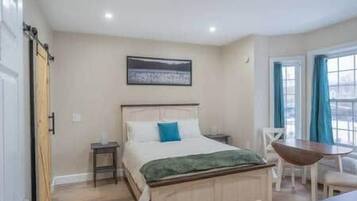 Quarto com cama, mesas de cabeceira, uma cadeira e uma mesa.
