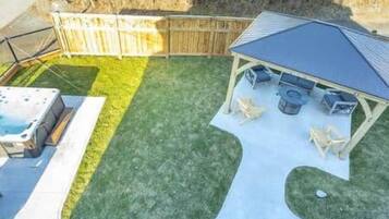 A backyard with a hot tub, a covered patio area, and a wooden fence.
