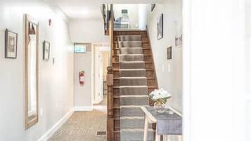 A hallway with a wooden staircase, a door at the end, and a small table with a vase.