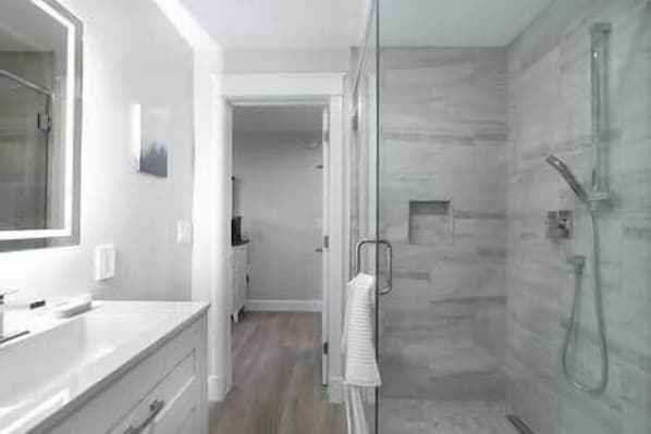 Une salle de bain moderne avec une douche à parois de verre, un grand miroir et un plan de toilette blanc.