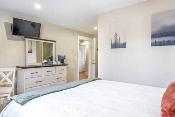 A bedroom with a bed, a dresser, a television mounted on the wall, and a door leading to another room.