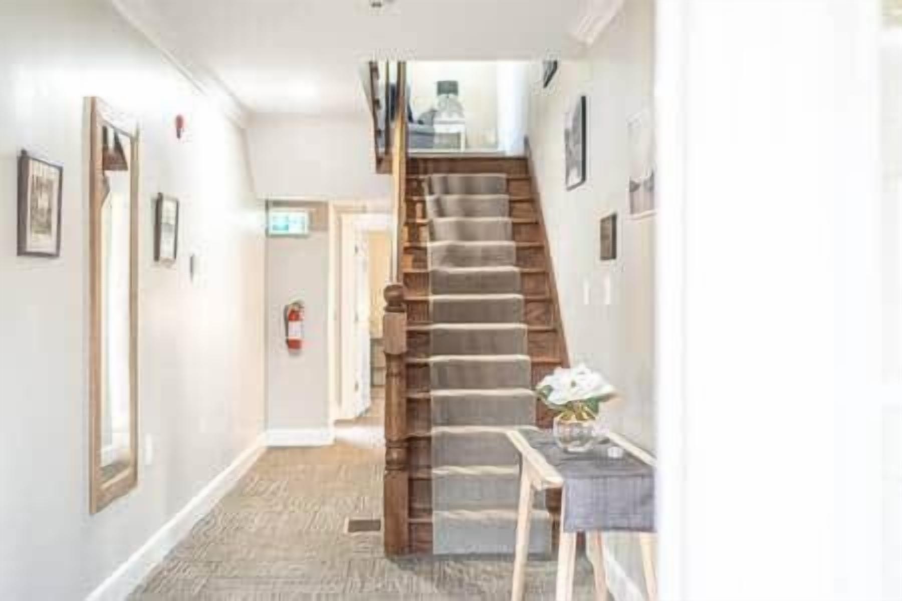 Un couloir avec un escalier en bois, une porte au fond et une petite table sur laquelle se trouve un vase.