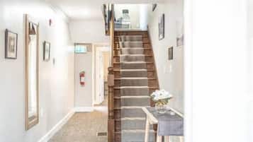 Un couloir avec un escalier en bois, une porte au fond et une petite table sur laquelle se trouve un vase.