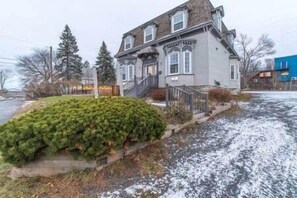 A two-story house with a front porch, a small garden, and a snow-covered driveway.