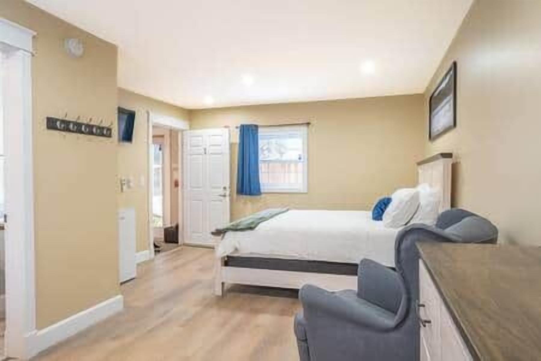 A bedroom with a bed, a desk, and a chair. There is a window with curtains, a door, and a wall-mounted sign.