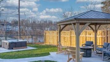 A covered outdoor seating area with a wooden structure, a hot tub, and a grill.