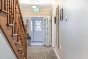 A hallway with a wooden staircase, a door with glass panels, and a light fixture on the ceiling. - Riverside Inn - Unit 2 Accessible (New Glasgow)