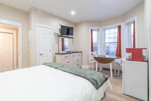 A bedroom with a bed, a desk, and a chair. There is a television on a stand and a window with curtains. - Riverside Inn - Unit 3 (New Glasgow)
