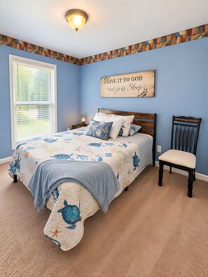 A bedroom with a bed, a chair, a nightstand, a wall clock, and a decorative sign.