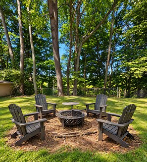A backyard with a circular fire pit surrounded by four Adirondack chairs.